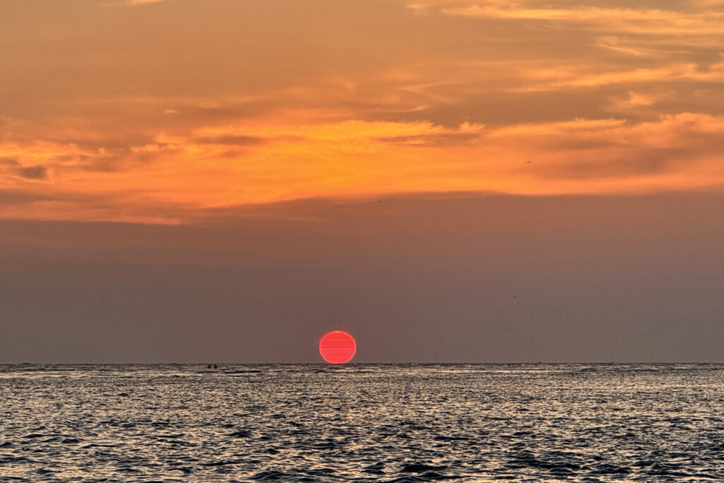 a photo taken by Captain Ricky Poupore aboard the Rock Bottom of SeaCo Fishing Charters while heading out for some of the best offshore fishing charters in St. Augustine, Florida, shows an deep hot pink sun, just barely over the horizon with a background of purple clouds and an orange sky above.